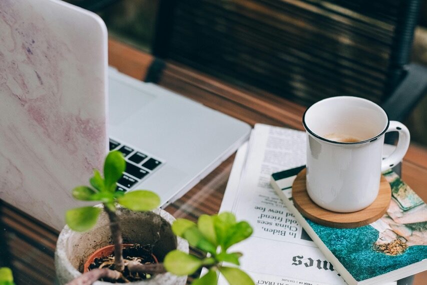 A digital gardener’s workspace with a laptop, coffee mug, and potted plant on a glass table in the garden, symbolizing balance between technology and nature.